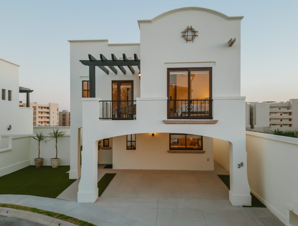 White two-story villa with arched driveway, balcony, and warm interior lights; house number 38 visible on the column.