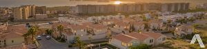 Encabezado | atlas desarrollos Atlas desarrollos coastal suburban neighborhood at sunset with rows of beige tile roof houses and palm trees and mid rise buildings along the shore the ocean is visible on the horizon